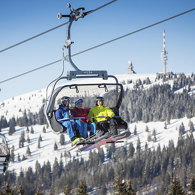 Drei Skifahrer im Sessellift, im Hintergrund der Feldberg